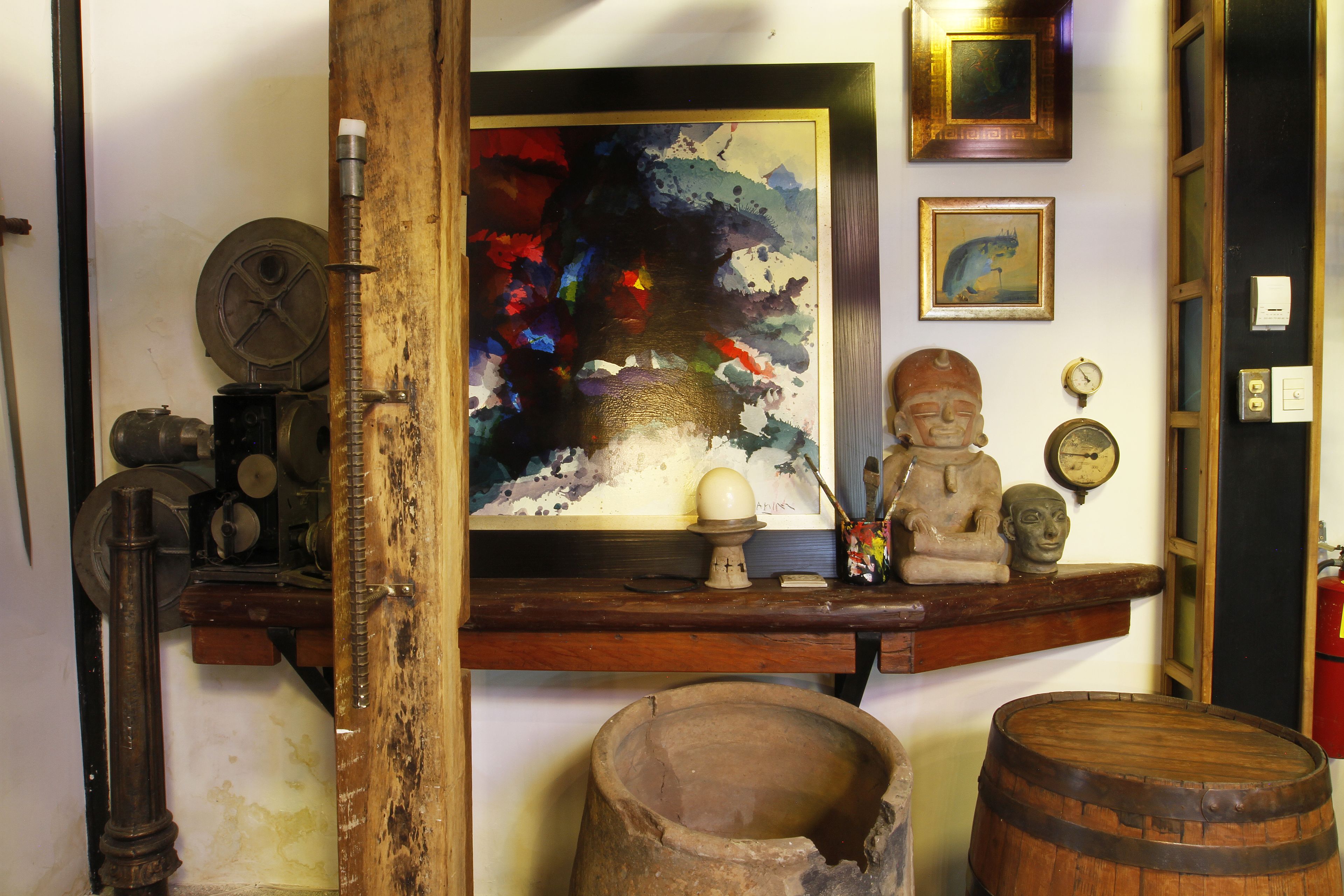 A room with a wooden shelf displaying various items, including a painting, a Buddha statue, and a clock.