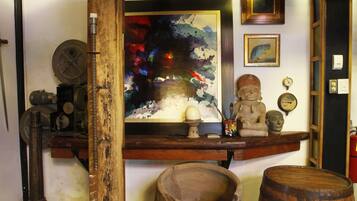 A room with a wooden shelf displaying various items, including a painting, a Buddha statue, and a clock.