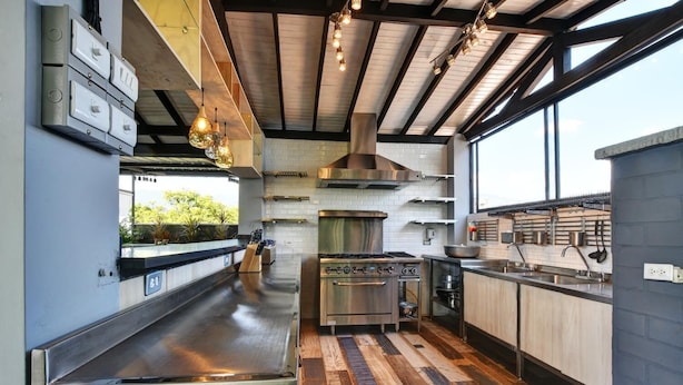 A modern kitchen with stainless steel appliances, a wooden floor, and a large window providing natural light.