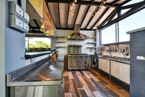 A modern kitchen with stainless steel appliances, a wooden floor, and a large window providing natural light. - International House Medellin - Hostel (Medellín)
