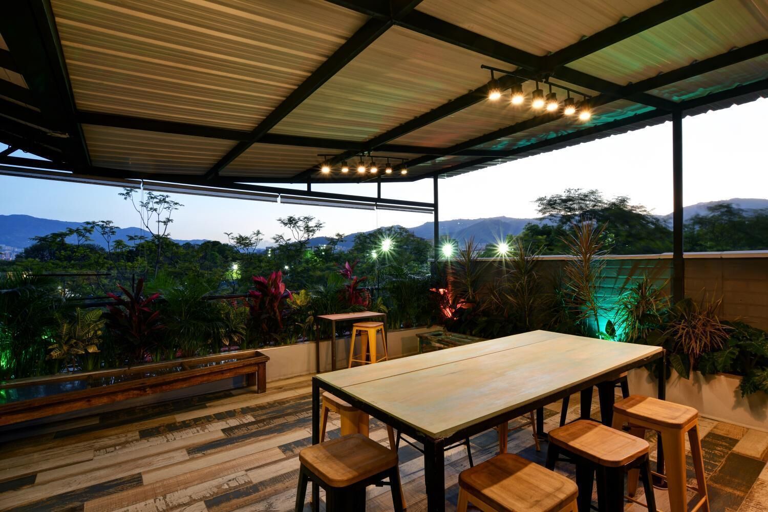 An outdoor dining area with a wooden table and chairs, surrounded by lush greenery and a view of distant mountains.