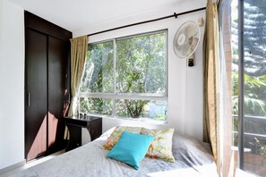 Ein Schlafzimmer mit Bett, Fenster, Ventilatoren und Kleiderschrank.