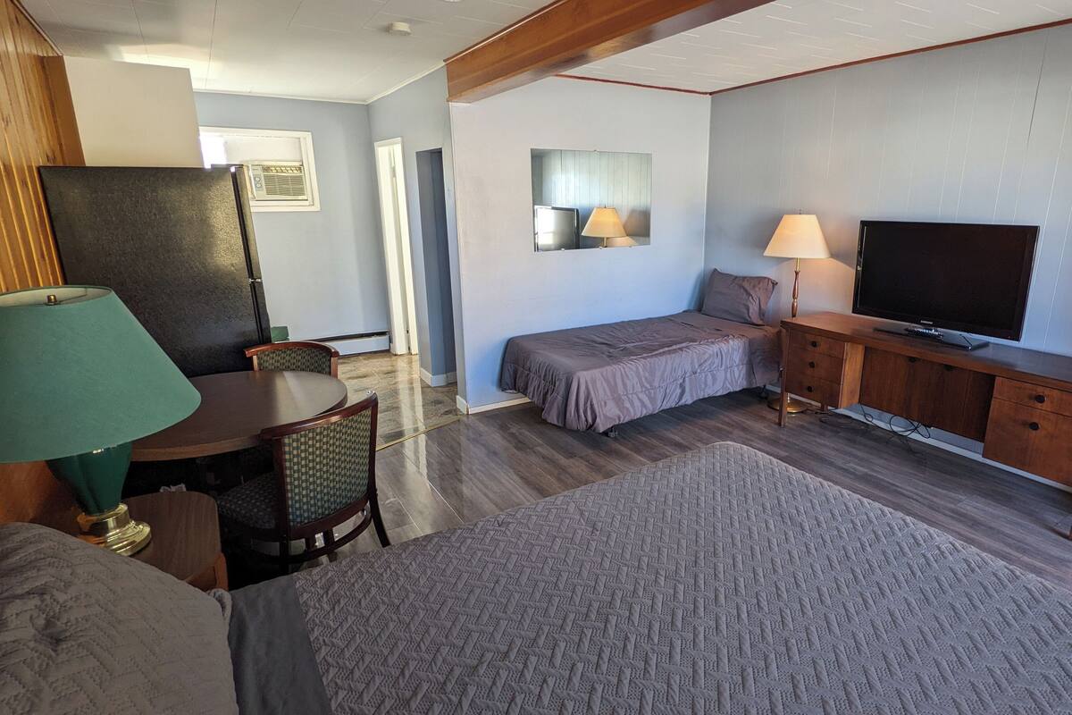 A compact room with a bed, a desk, a television, and a lamp.