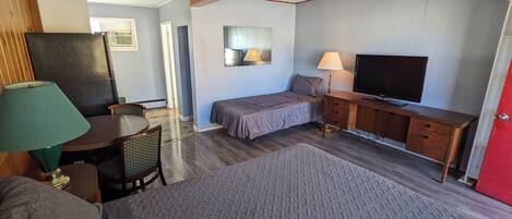A compact room with a bed, a desk, a television, and a lamp.