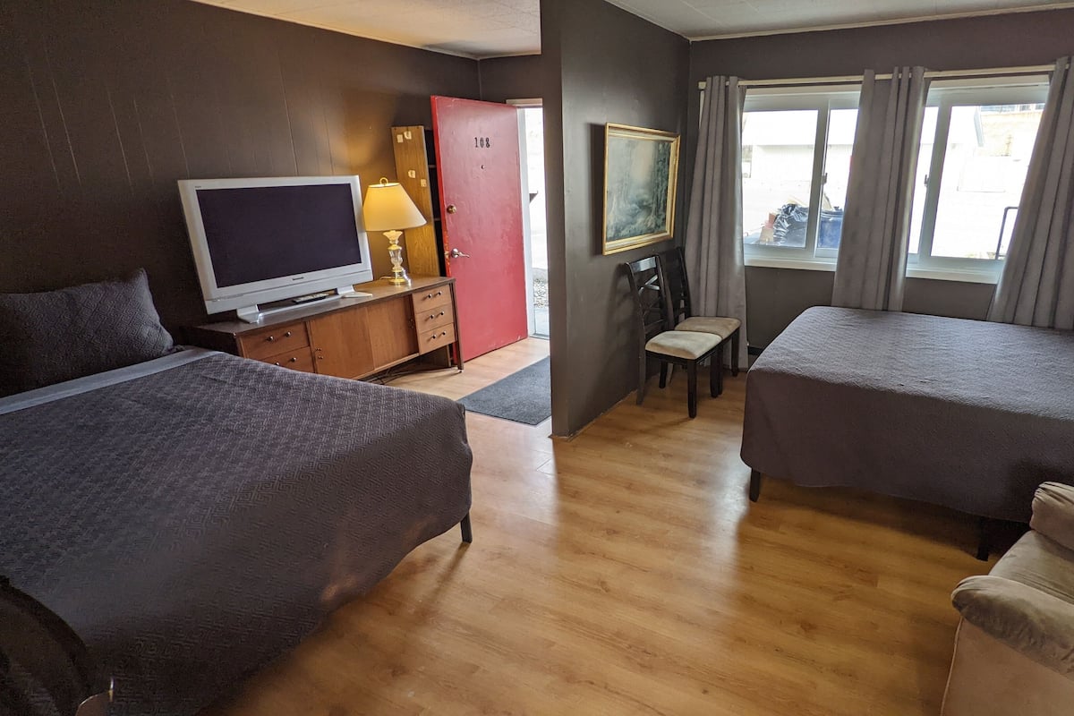A hotel room with two single beds, a TV, a desk with a lamp, a chair, and a window with curtains.