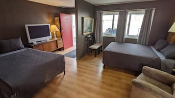 Habitación de hotel con dos camas individuales, televisor, escritorio con lámpara, una silla y ventana con cortinas.