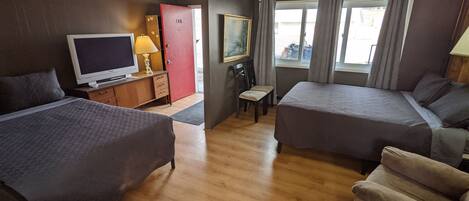 Habitación de hotel con dos camas individuales, televisor, escritorio con lámpara, una silla y ventana con cortinas.