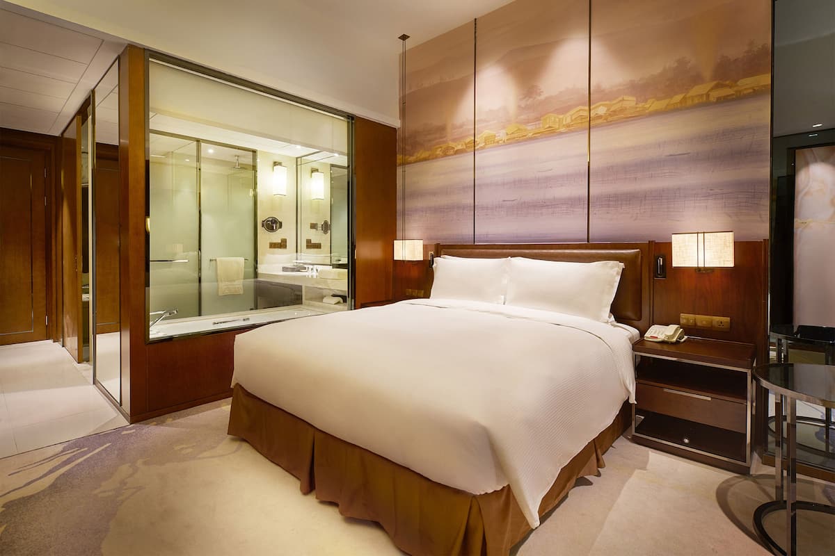Une chambre d’hôtel dotée d’un grand lit, d’une douche en verre, d’une coiffeuse avec un miroir et d’un téléviseur fixé au mur.