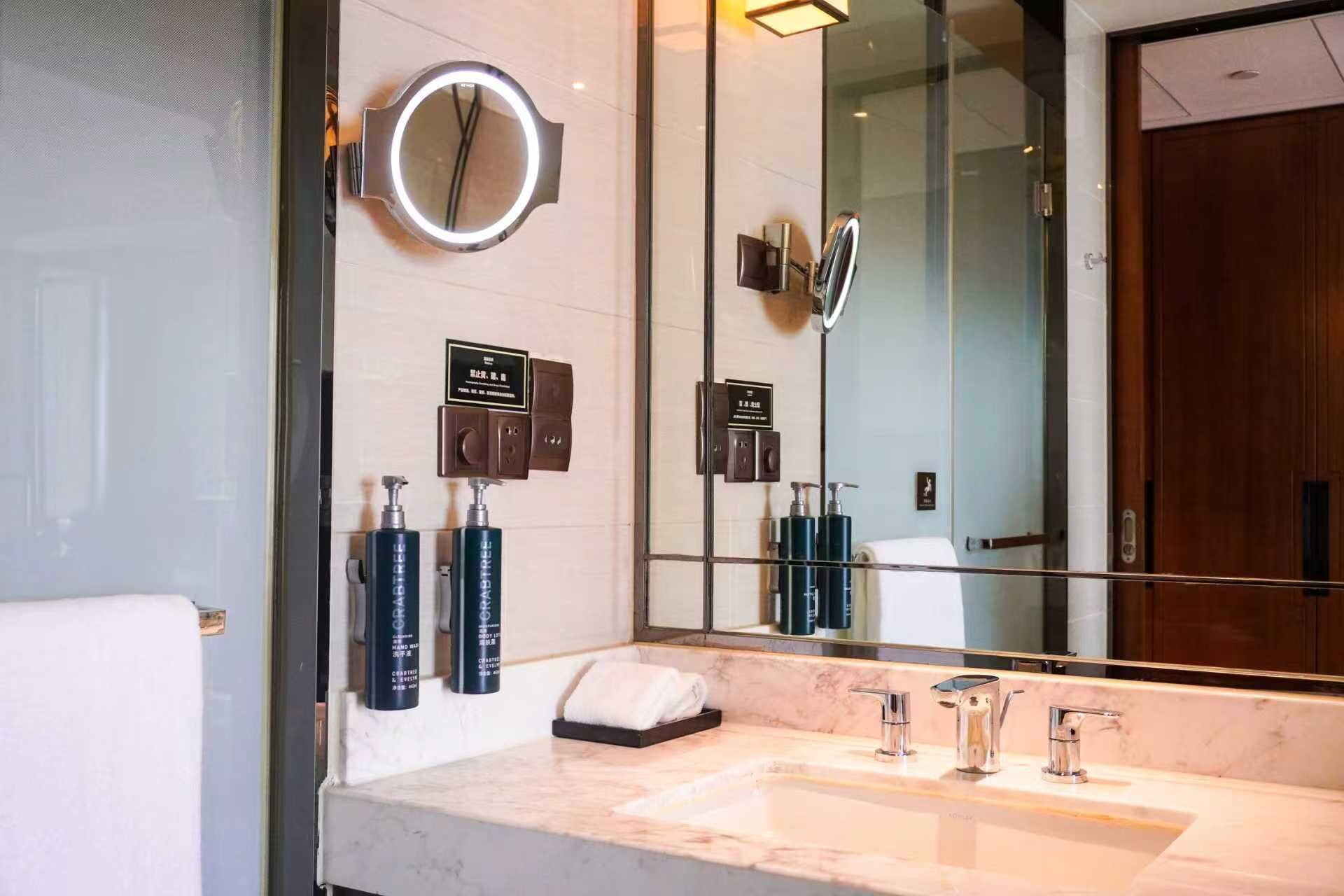 A modern bathroom with a large mirror, a round vanity mirror, and a marble sink.