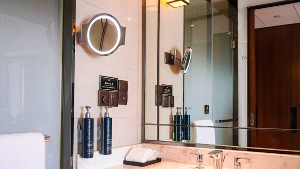 A modern bathroom with a large mirror, a round vanity mirror, and a marble sink.