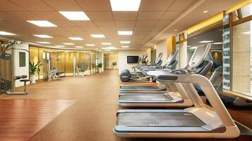 Een sportschool met loopbanden, fitnessapparatuur en een groot raam.