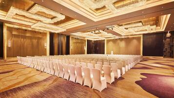 Un amplio salón de conferencias con filas de sillas blancas, una alfombra estampada y candelabros decorados.
