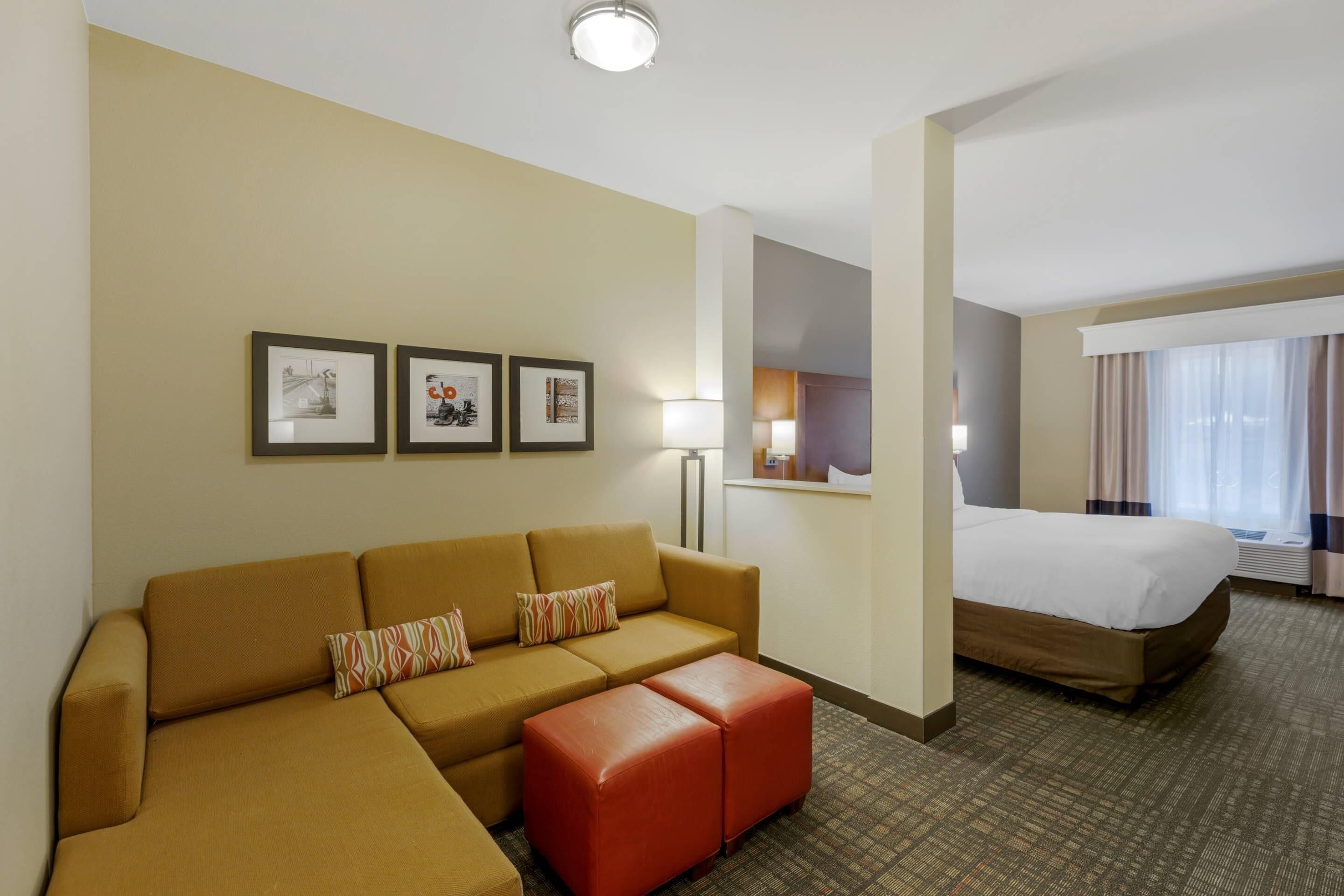 Een hotelkamer met een bank, voetenbankje, bed en ingelijste foto’s aan de muur.