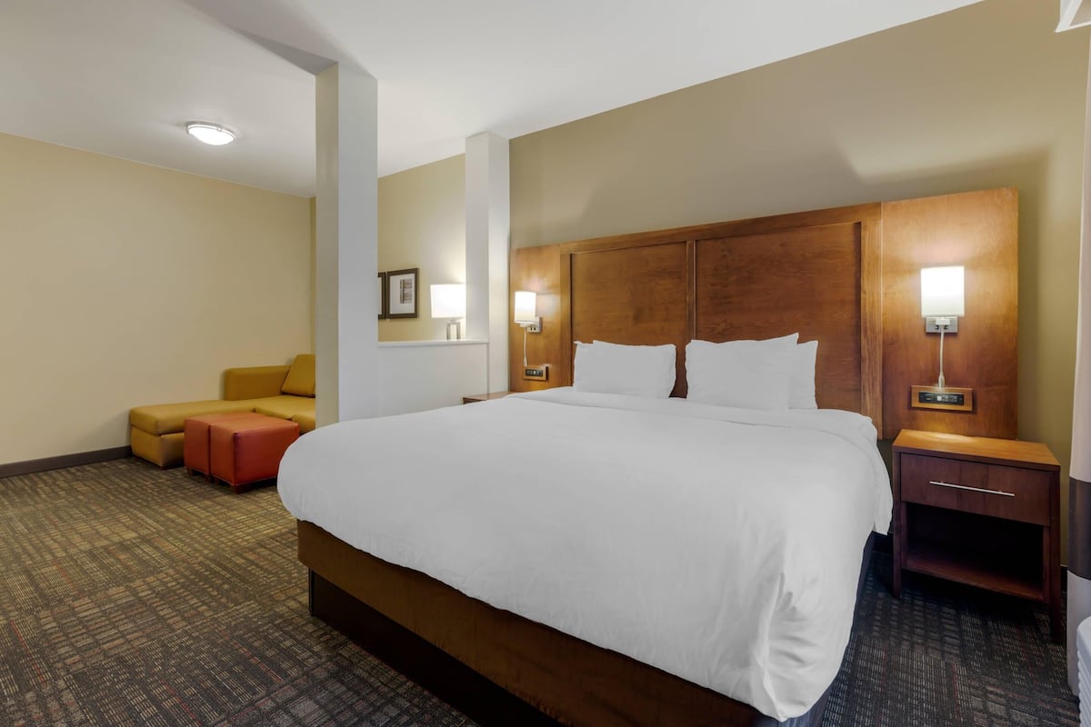A hotel room with a large bed, a wooden headboard, bedside lamps, a small sofa, and a carpeted floor.