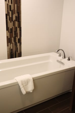 Bathroom features a rectangular bathtub with a faucet and handheld showerhead, alongside a mosaic tile design and dark wooden floor.