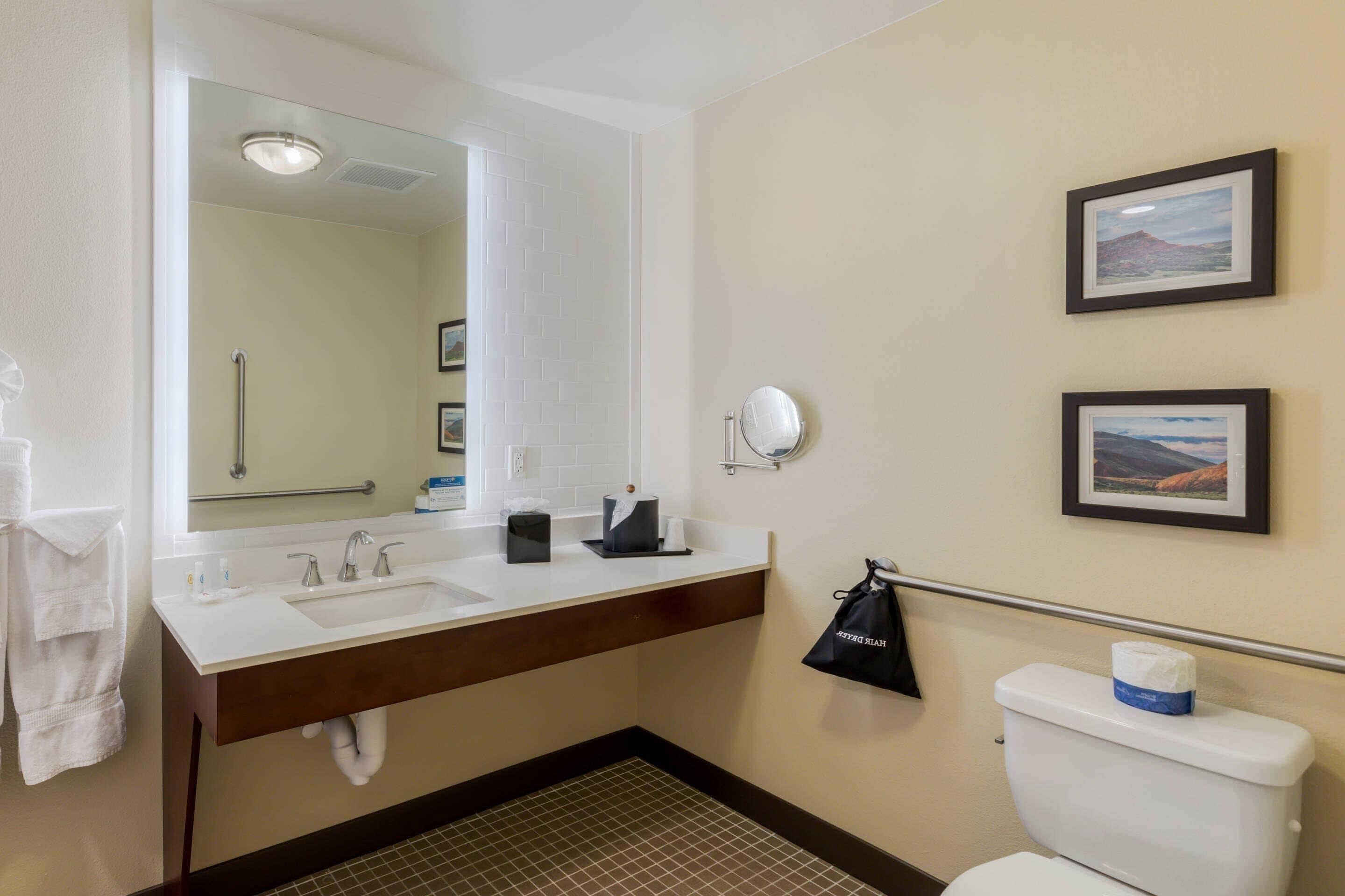 A bathroom with a white sink, mirror, and toilet, a towel rack, and two framed pictures on the wall.