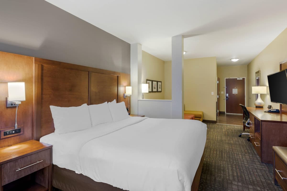 A hotel room with a large bed, wooden headboard, bedside tables with lamps, a desk with a chair, and a television.