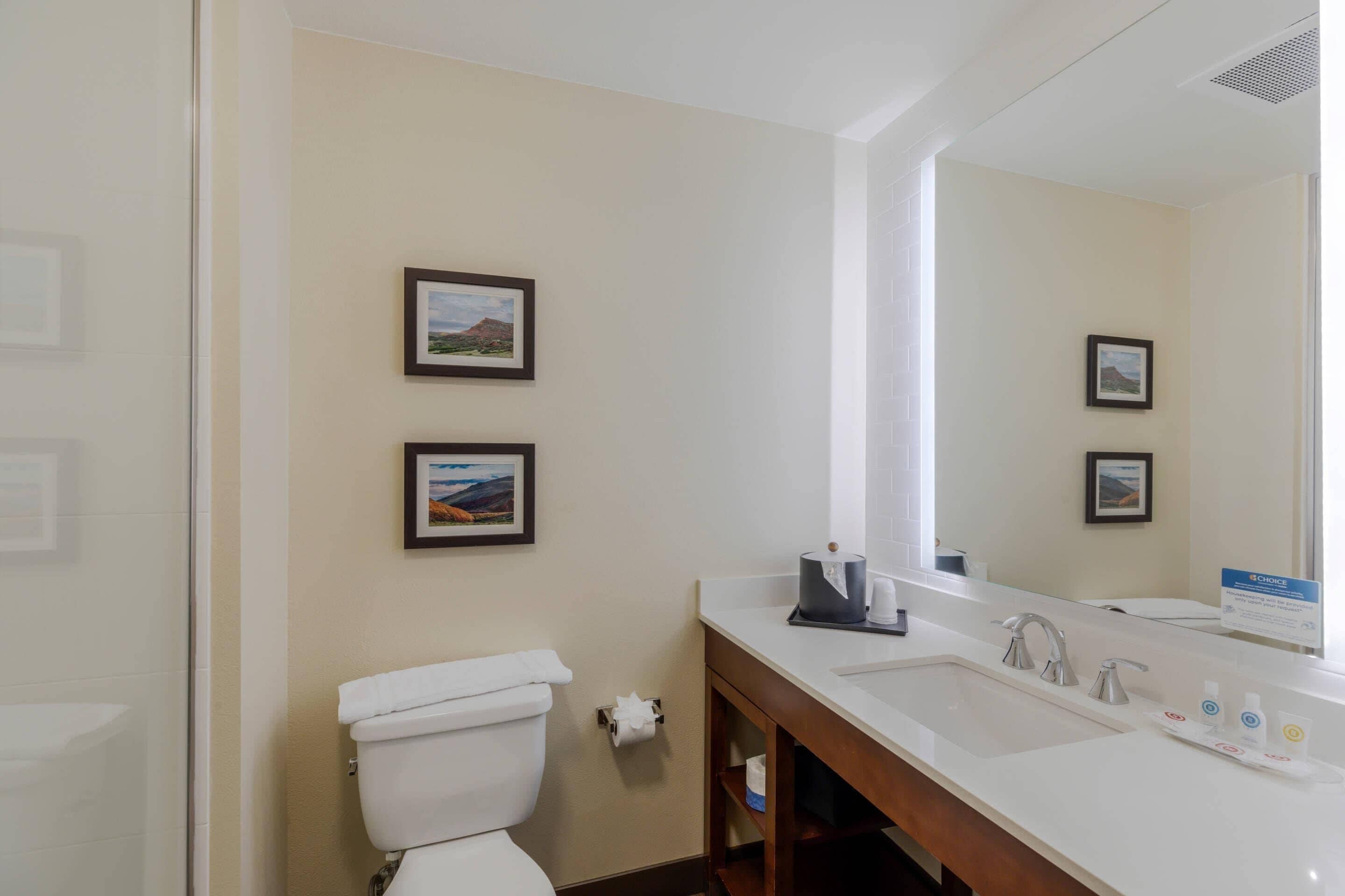 Une salle de bain d’hôtel avec des toilettes, un lavabo et deux tableaux encadrés accrochés au mur.
