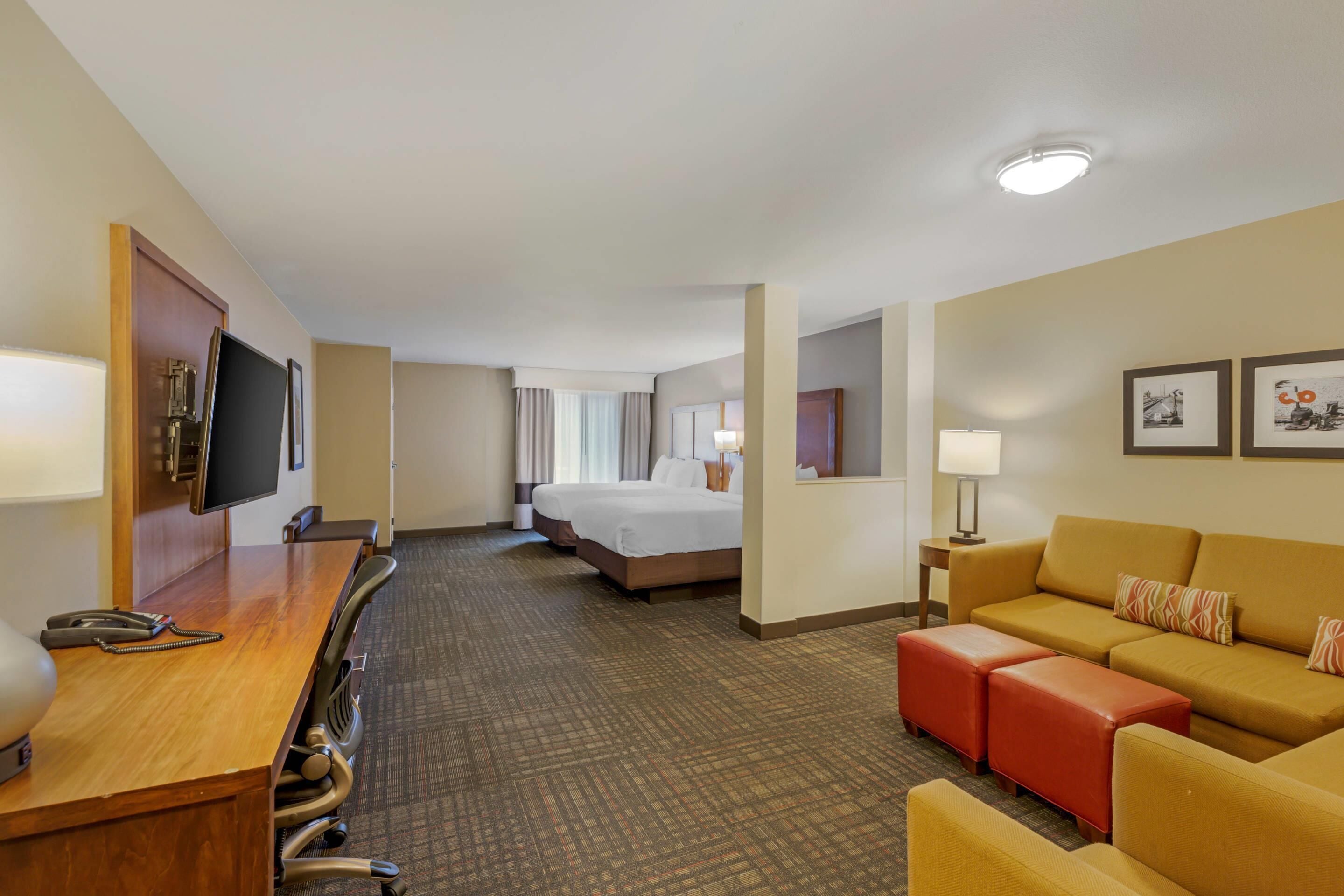 A hotel room with a wooden desk, a television, a bed, a sofa, and a carpeted floor.