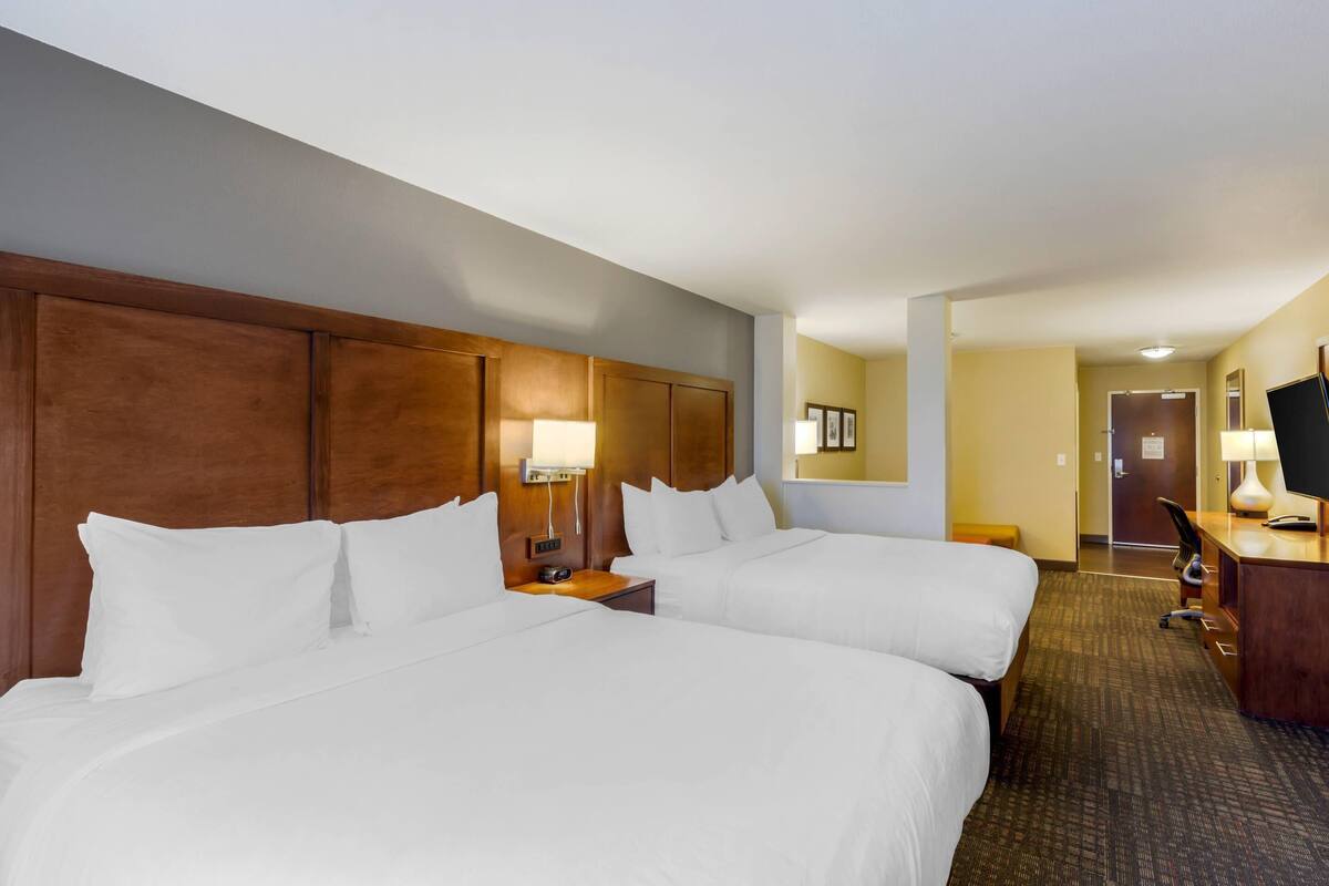 A hotel room with two beds, a desk, a chair, a lamp, and a television.