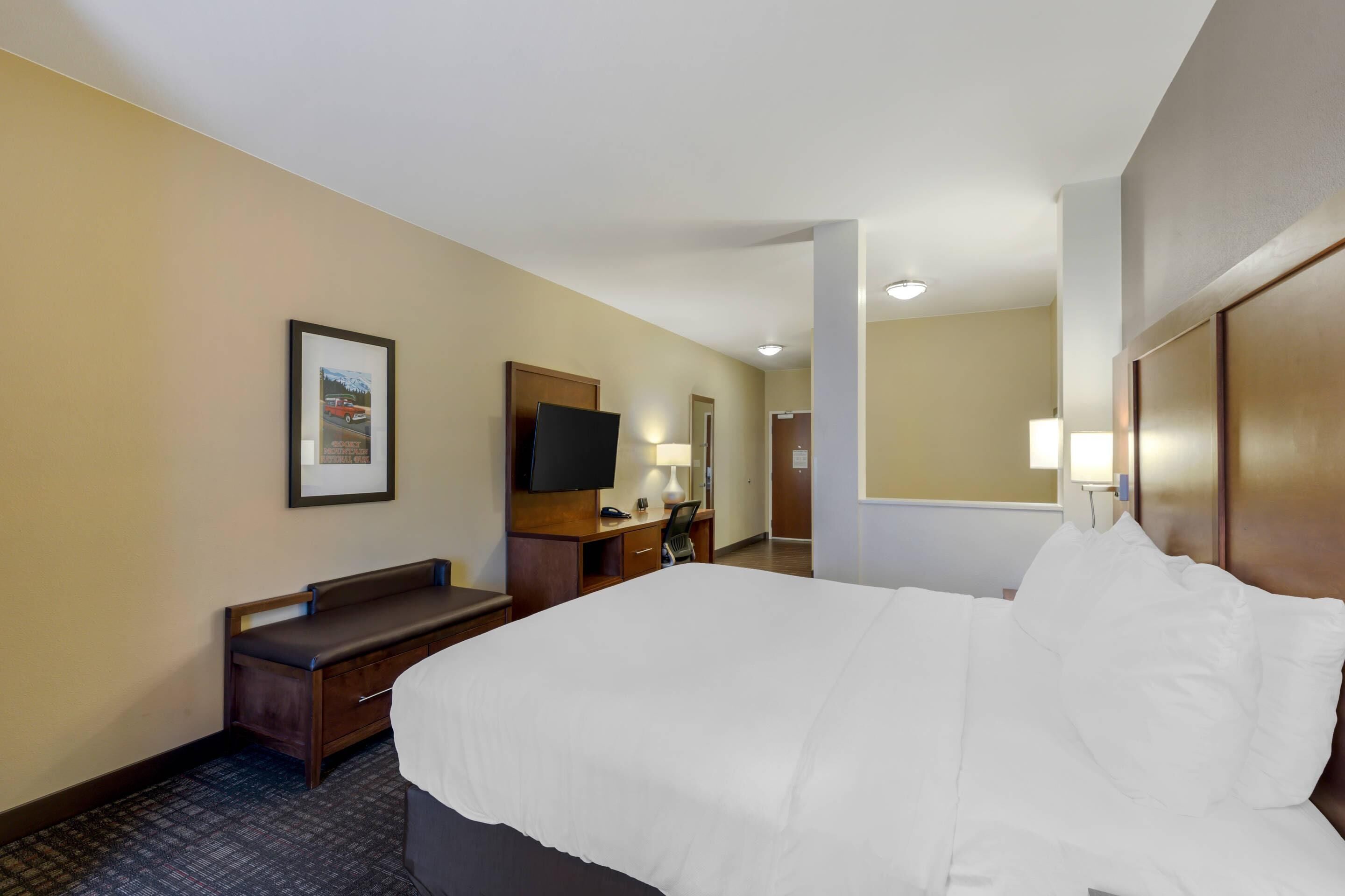 Quarto de hotel com uma cama, uma mesa com cadeira, uma televisão e um espelho.