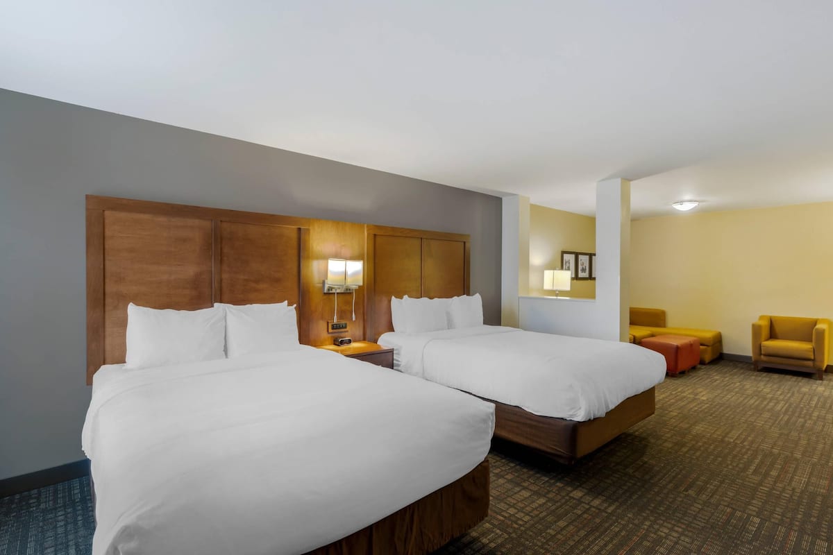 A hotel room with two beds, a nightstand, a lamp, a chair, and a small table.