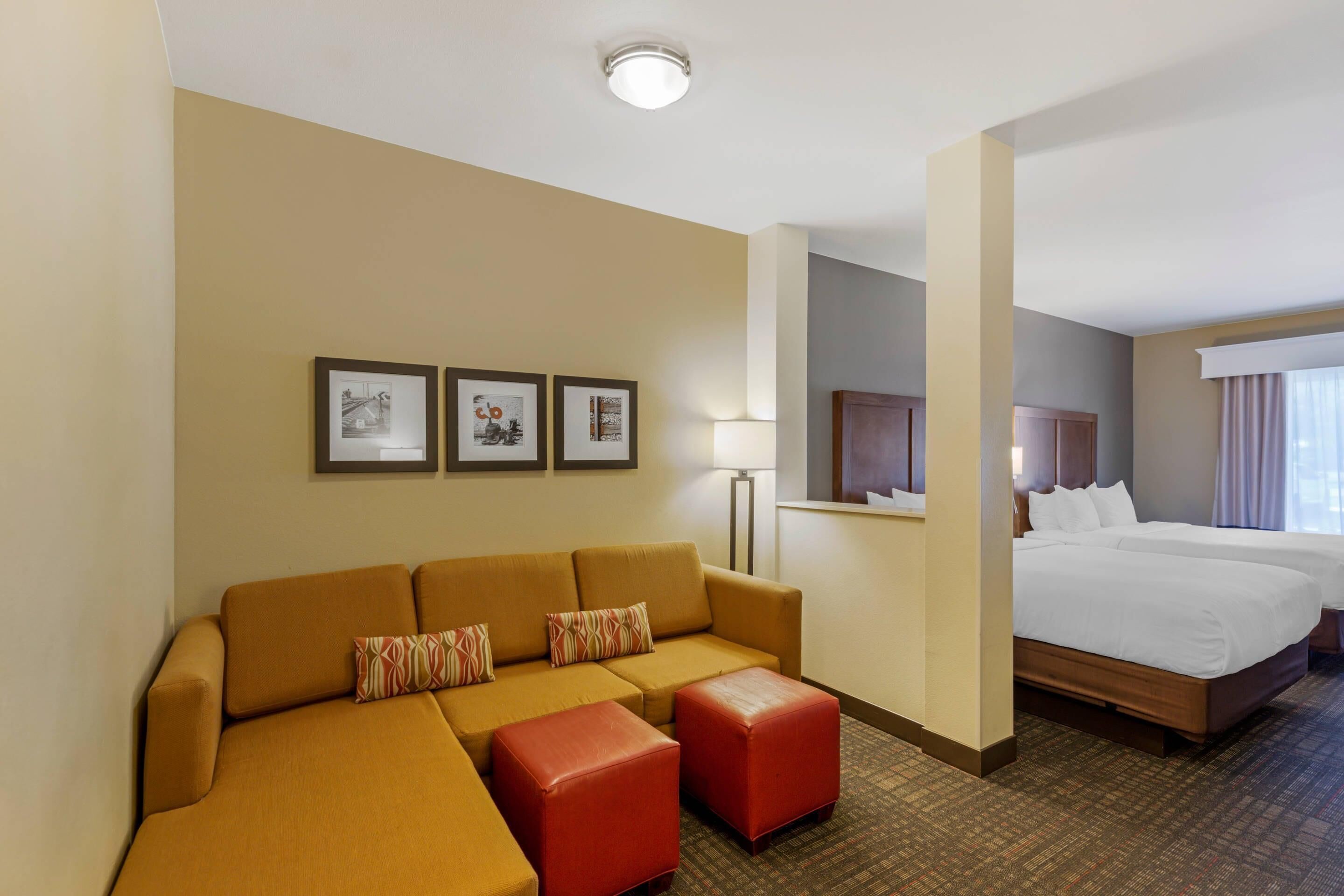 A hotel room with a sofa, ottomans, a bed, and framed pictures on the wall.