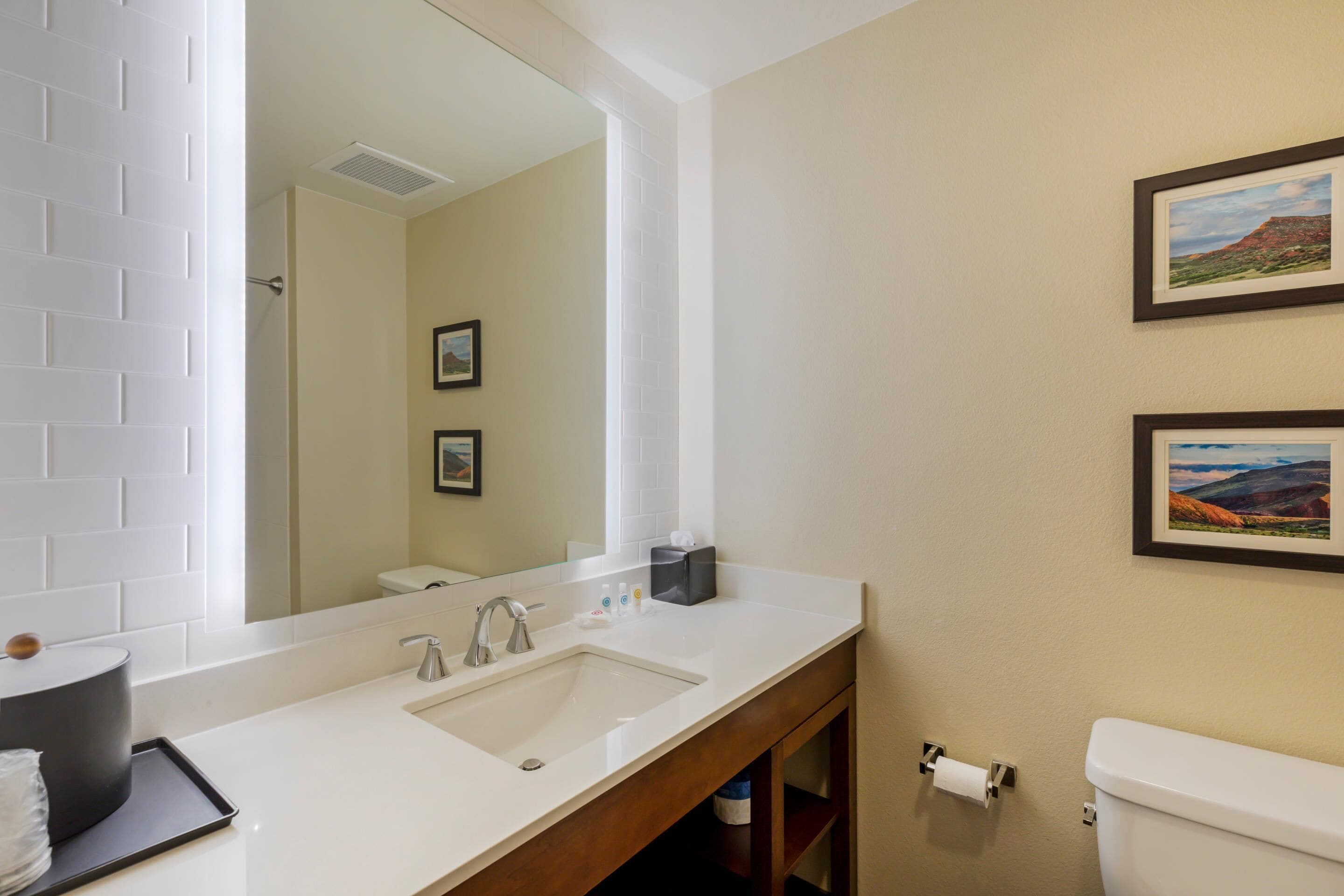A bathroom with a white sink, mirror, and toilet. There are framed pictures on the wall and a towel rack.