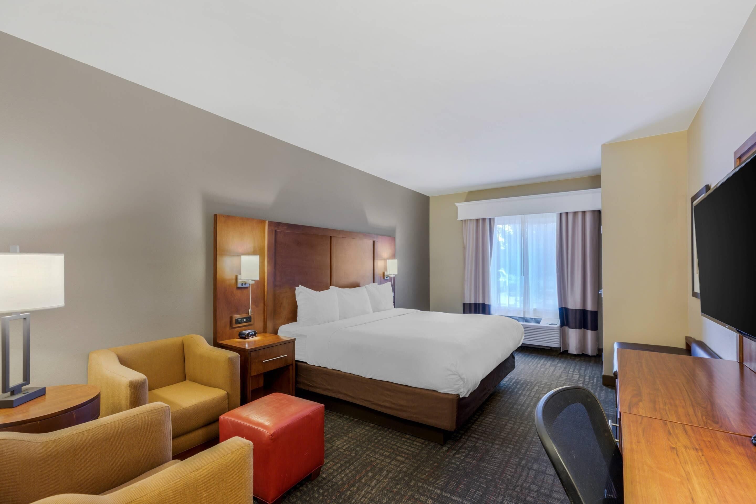 A hotel room with a bed, a desk, a chair, a TV, and a window with curtains.