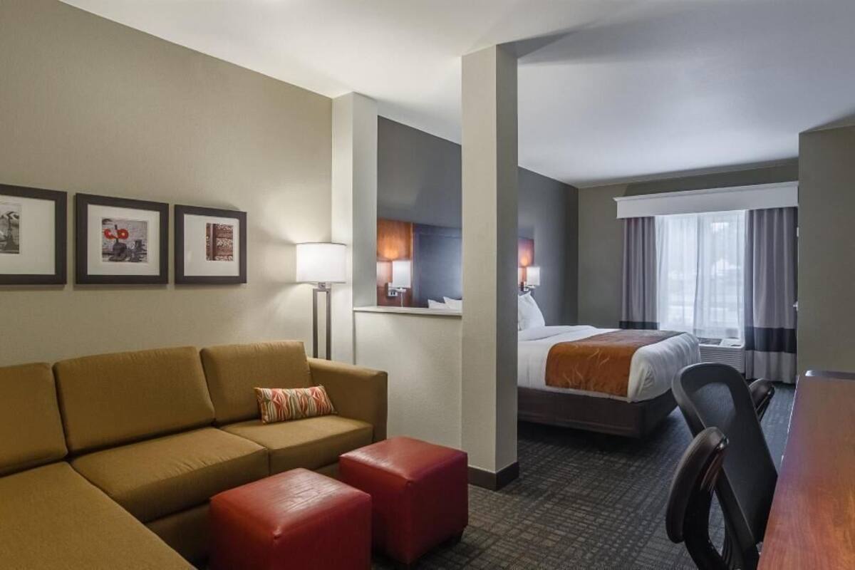 A hotel room with a sofa, ottoman, bed, desk, and a view of the city.