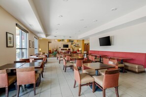 A spacious dining area with multiple tables and chairs, a flat-screen TV mounted on the wall, and a red cushioned seating area. - Comfort Suites Loveland (Loveland)
