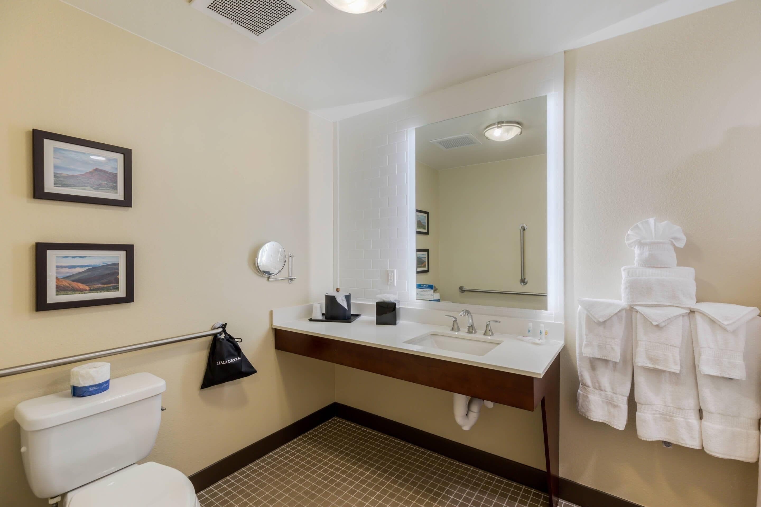 A bathroom with a toilet, sink, mirror, towel rack, and framed pictures on the wall.