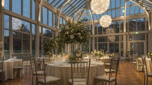 A spacious greenhouse with high ceilings and large windows, featuring elegant round tables and chairs, and ornate chandeliers. - Embassy Suites by Hilton Berkeley Heights (Berkeley Heights)