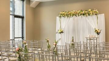 Una habitación con filas de sillas grises dispuestas para un evento, un ventanal grande y un fondo floral.