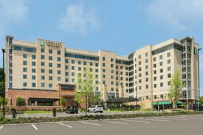 A large hotel with multiple floors, a prominent "Embassy Suites" sign, a "Grain & Canine" restaurant, and a parking lot with cars. - Embassy Suites by Hilton Berkeley Heights (Berkeley Heights)