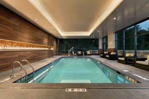 A modern indoor pool with clear water, a wooden wall, and a seating area with sofas and chairs. - Embassy Suites by Hilton Berkeley Heights (Berkeley Heights)