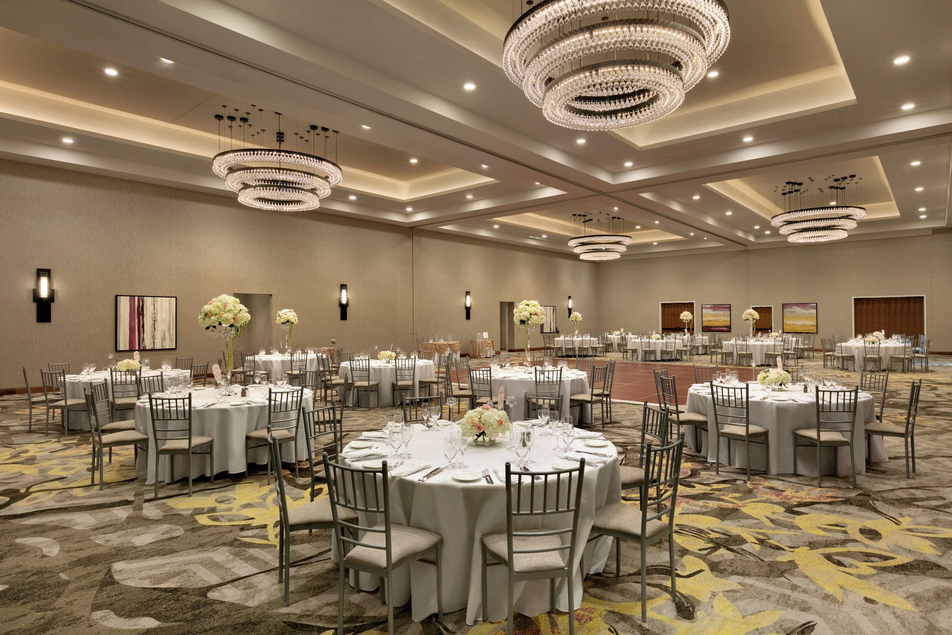 A large banquet hall with round tables, chairs, and chandeliers.