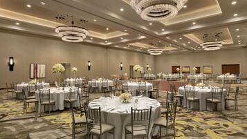 A large banquet hall with round tables, chairs, and chandeliers.