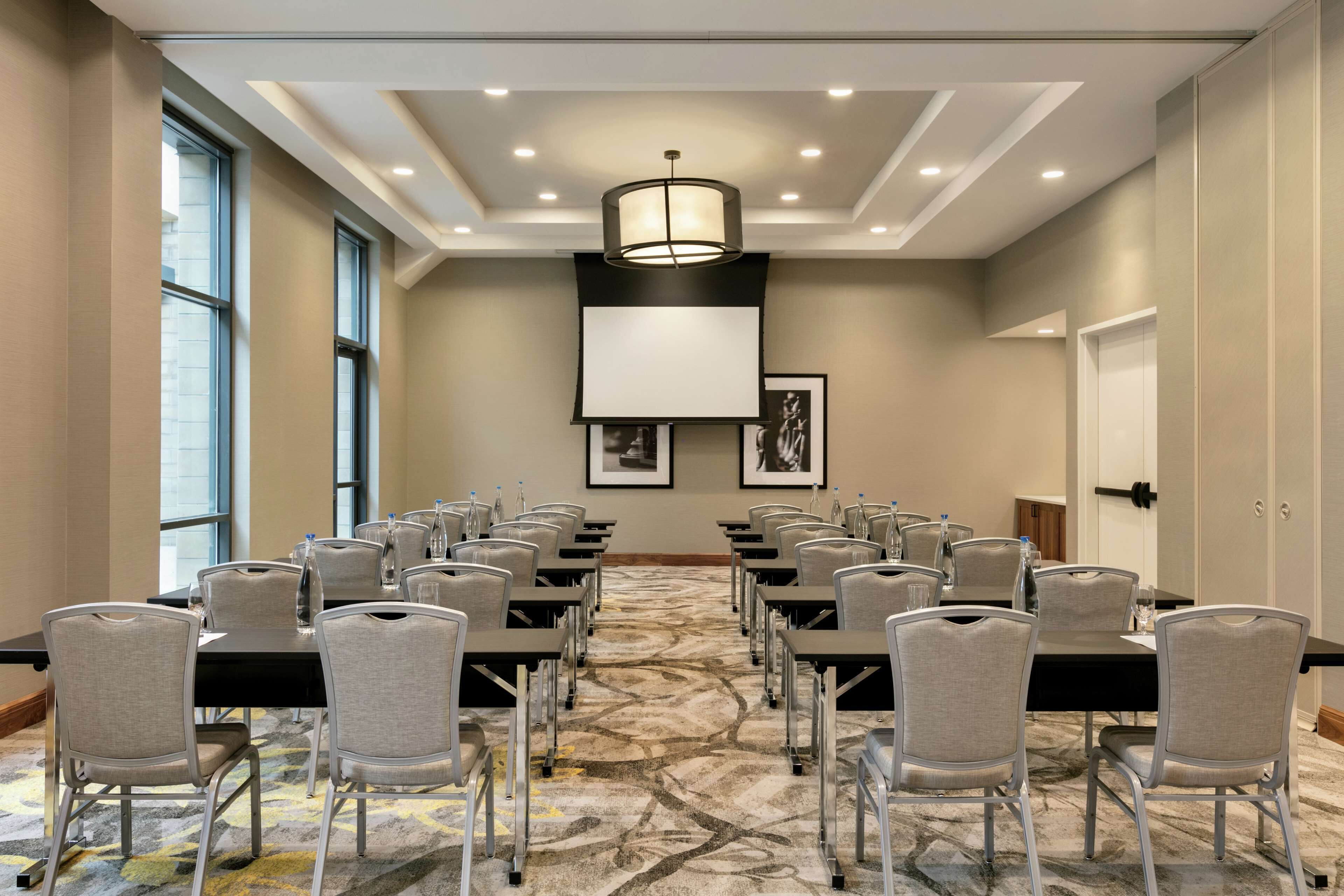 A conference room with rows of tables and chairs, large windows, and a patterned carpet.