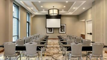A conference room with rows of tables and chairs, large windows, and a patterned carpet.