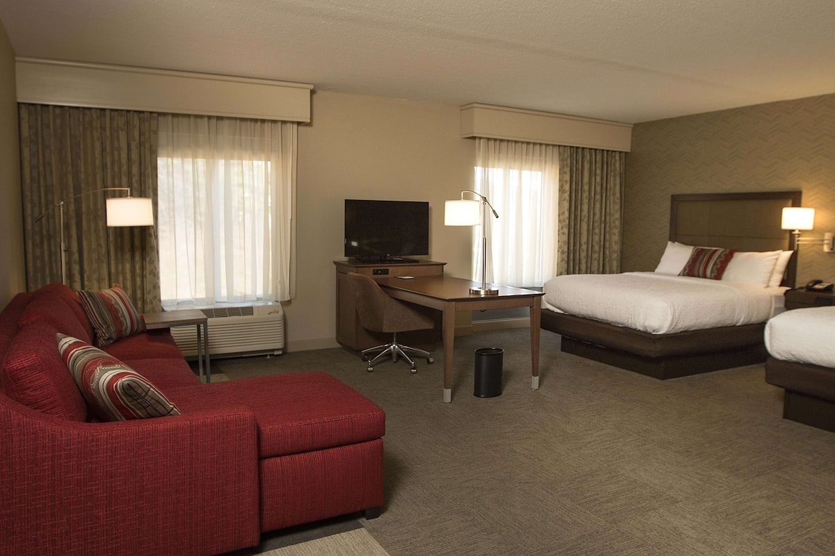 A hotel room with a red sofa, a bed, a desk with a television, and a lamp.