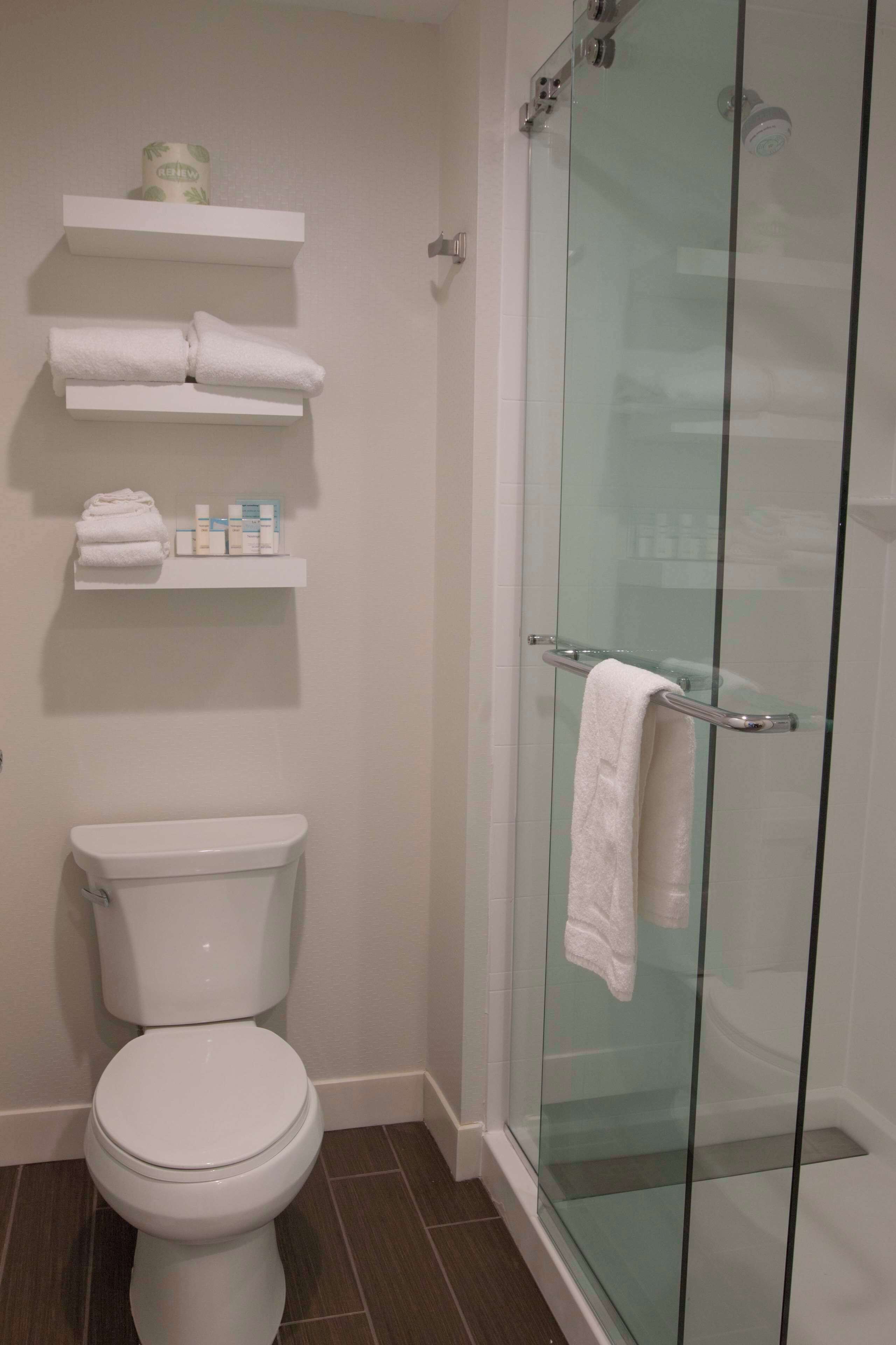 Un baño con inodoro, cabina de ducha de vidrio y repisas con artículos de aseo.