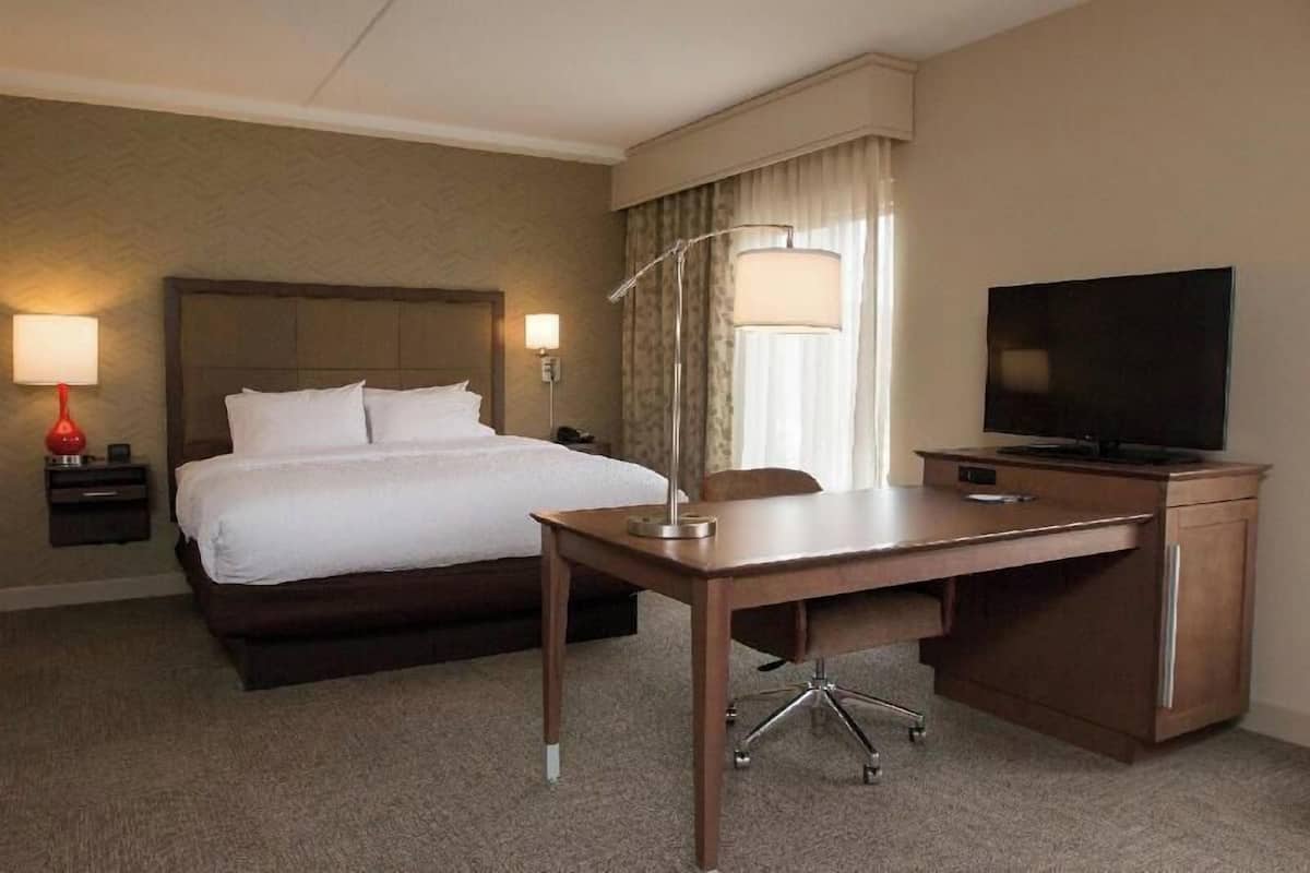 A hotel room with a bed, desk, chair, lamp, TV, and curtains.
