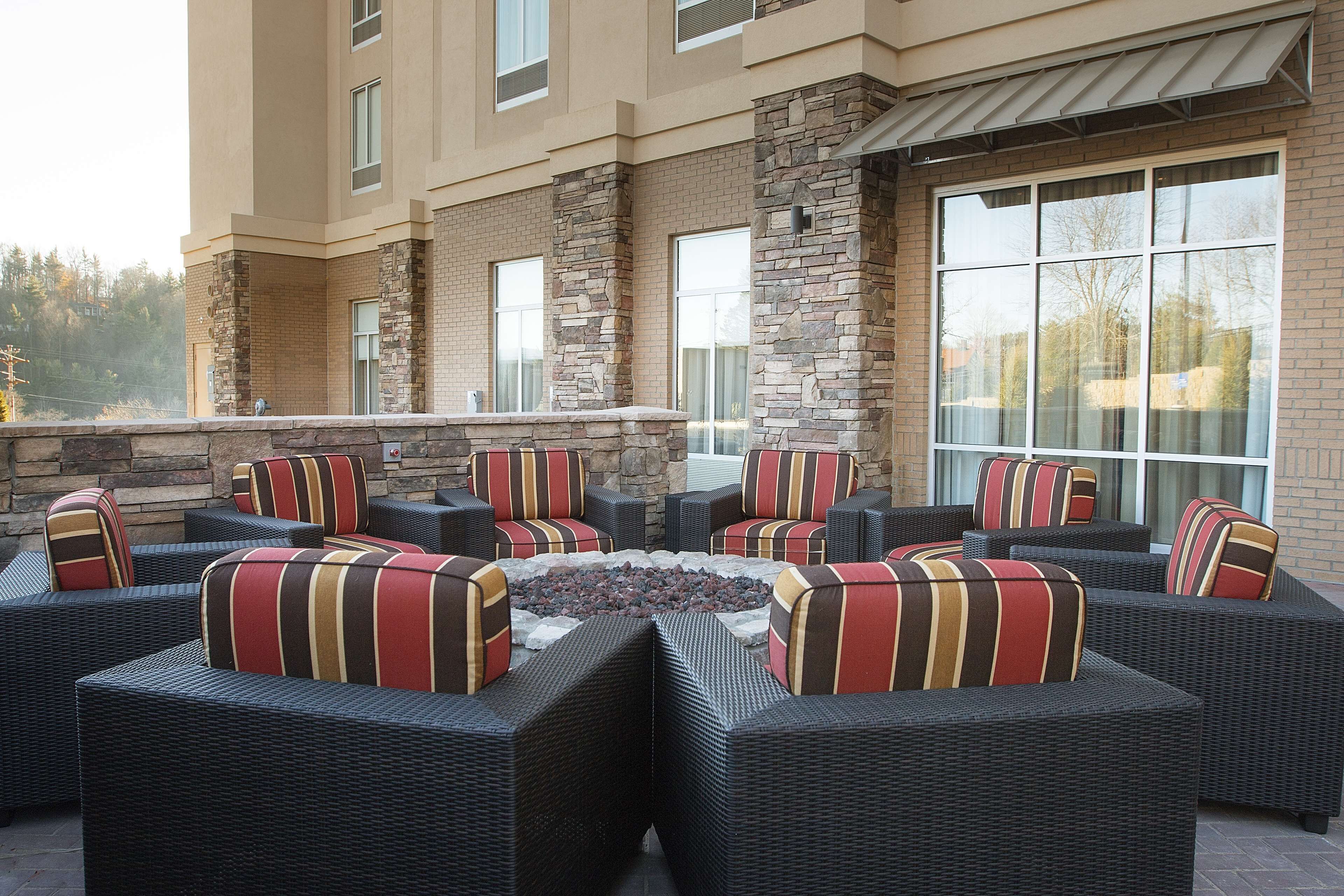 An outdoor seating area with wicker furniture and striped cushions, a fire pit, and a stone wall.