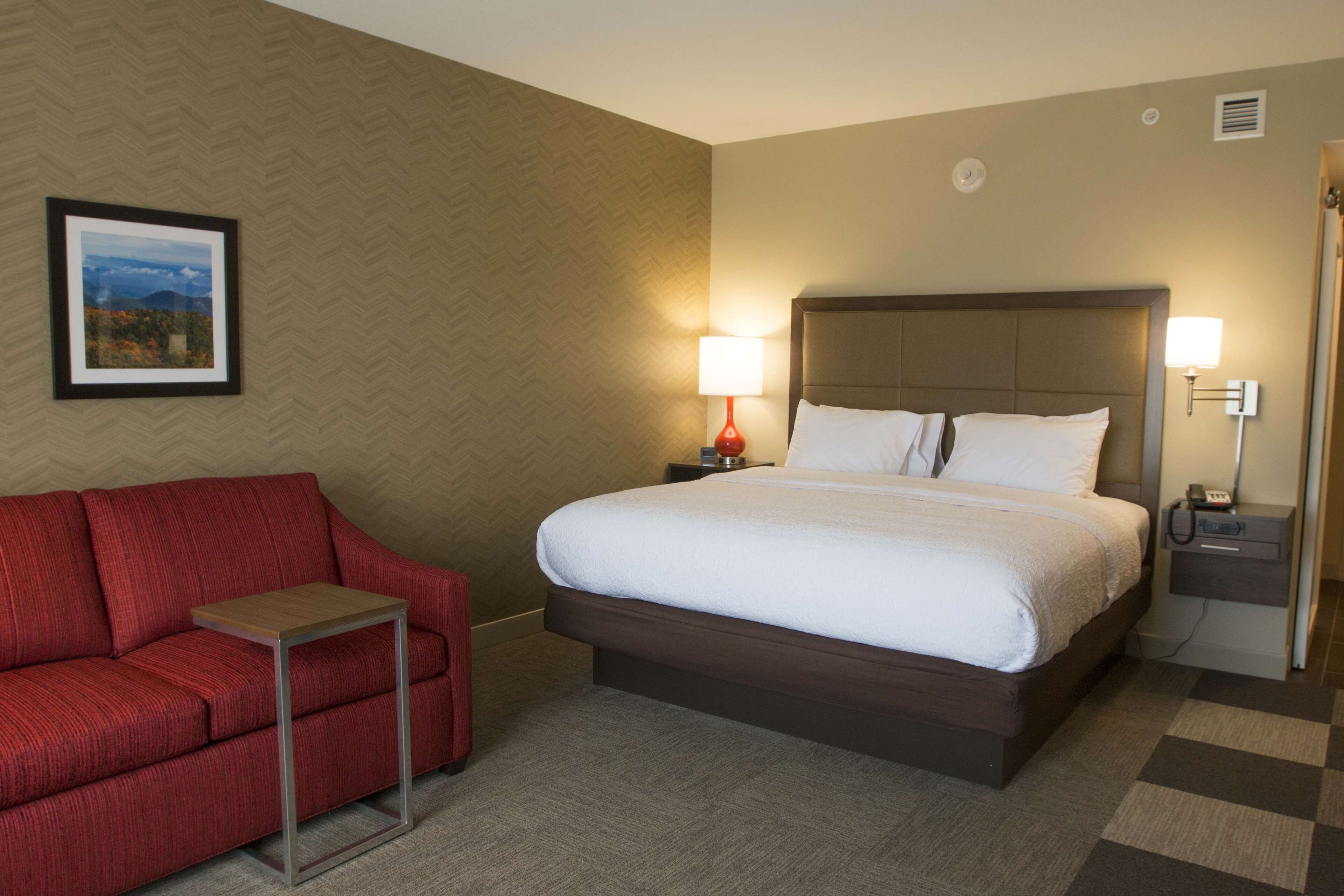 Een hotelkamer met een groot bed, een rode bank, een tafeltje en een nachtkastje met een lamp.