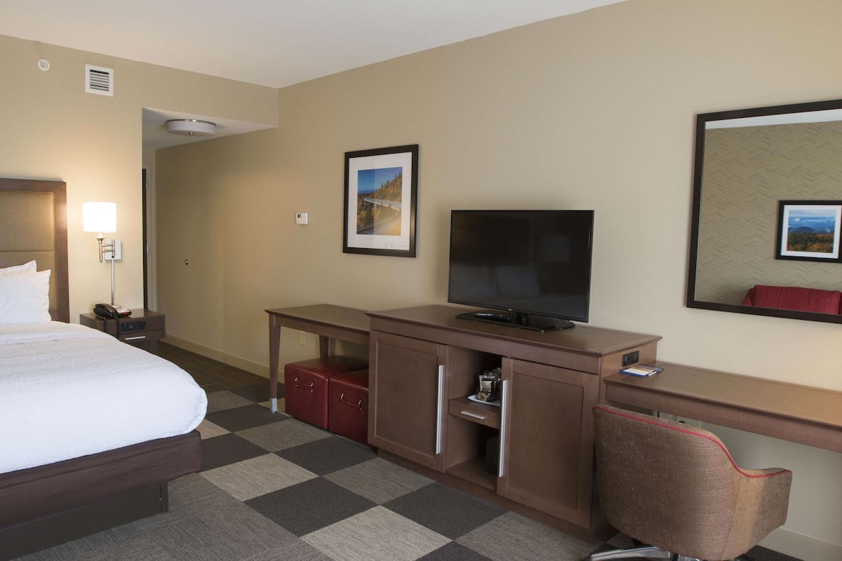 A hotel room with a bed, a desk with a television, a chair, and a small cabinet.