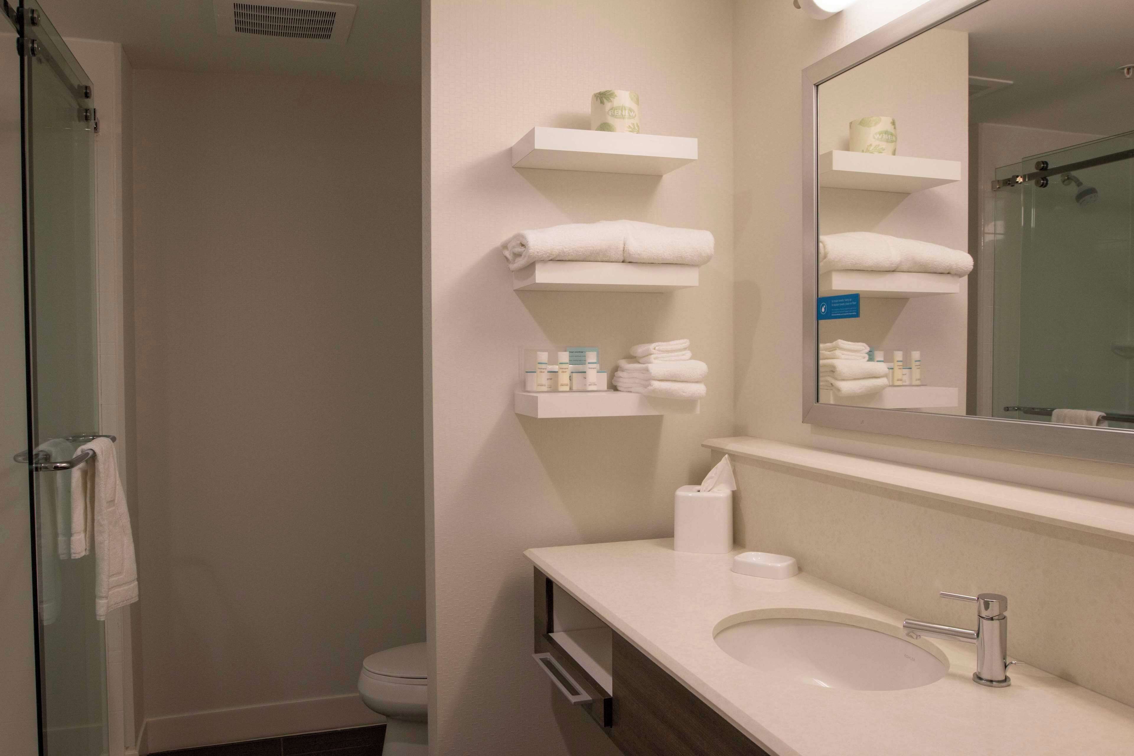 A bathroom with a glass shower enclosure, a sink with a mirror, and shelves with towels and toiletries.