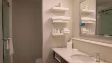 A bathroom with a glass shower enclosure, a sink with a mirror, and shelves with towels and toiletries.