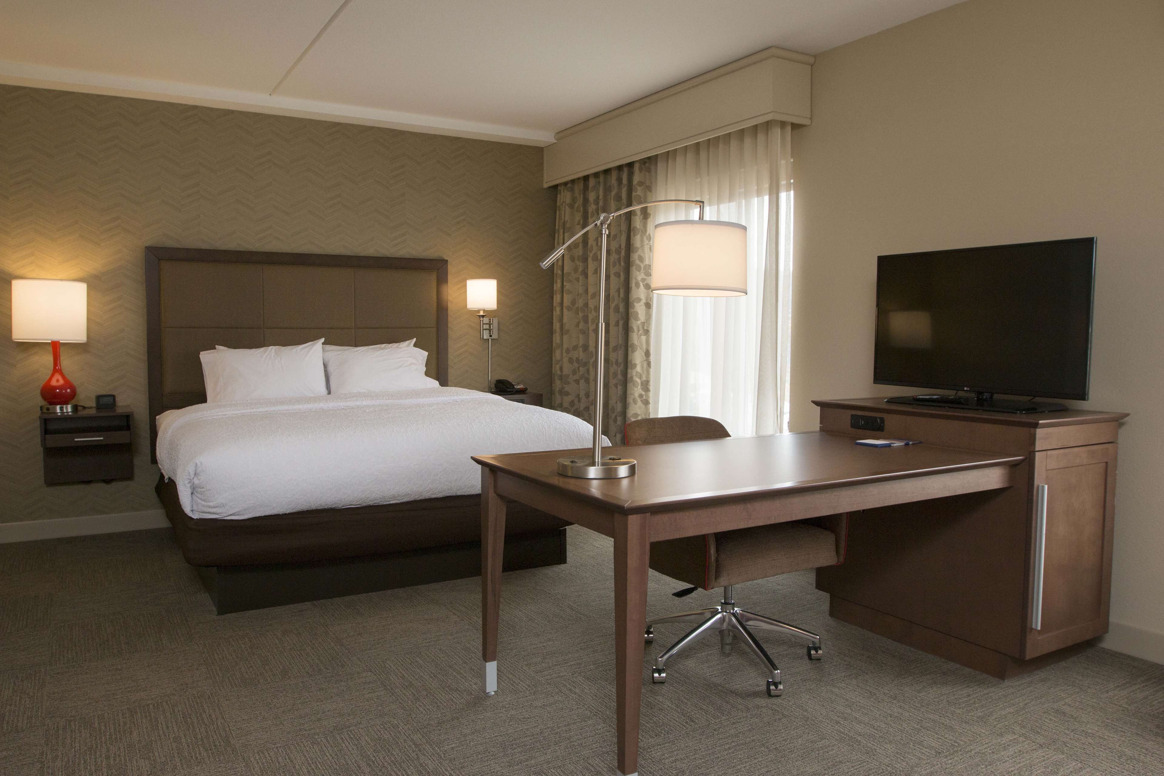 Una habitación de hotel con cama, escritorio, silla, televisor, lámpara y mesita de noche.