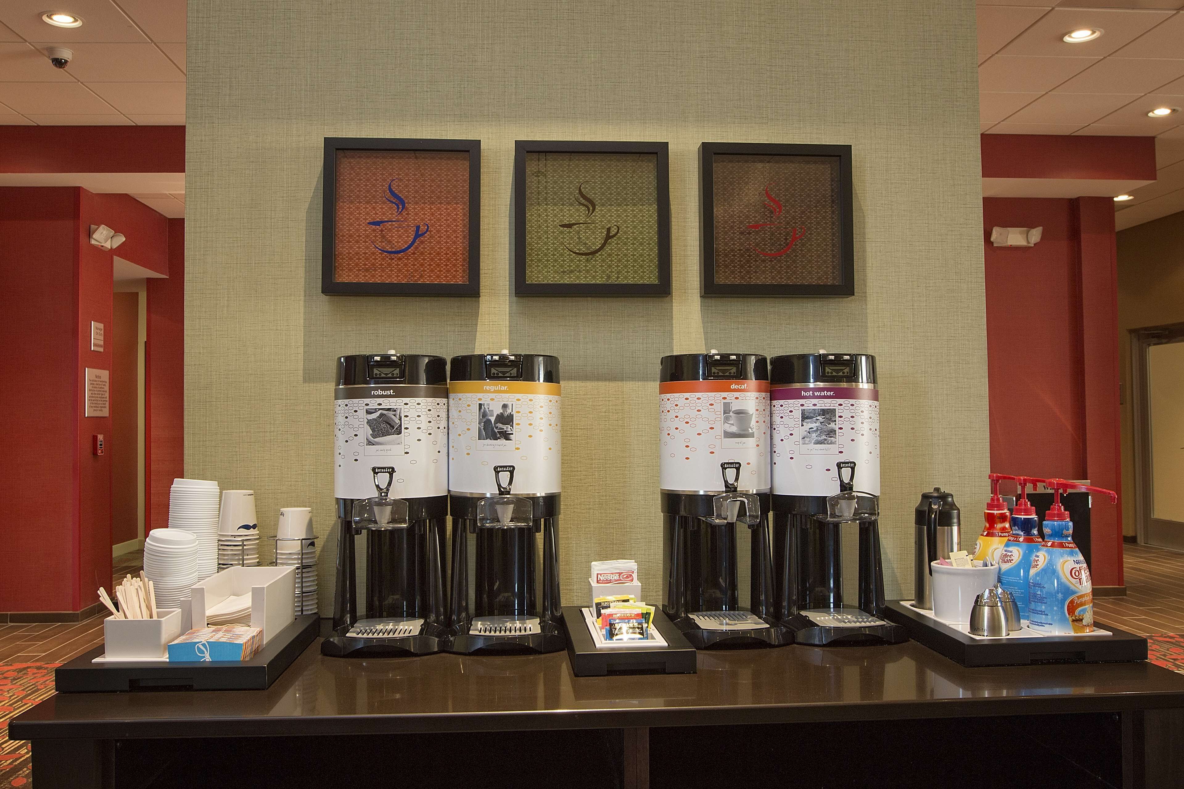 A coffee station with four coffee makers, disposable cups, and a beverage dispenser.